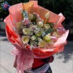 Beautiful Mix Bouquet for gift with cream roses, pink tulips, gypsophila and eucalyptus in coral-pink wrapping.