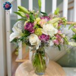 Mix Bouquet 031 with white lilies, ivory and mauve roses, pink flowers and greenery in a glass vase