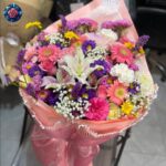 Mix Bouquet 039 with pink gerberas, white lilies, roses, purple flowers and baby's breath in coral-pink wrapping.